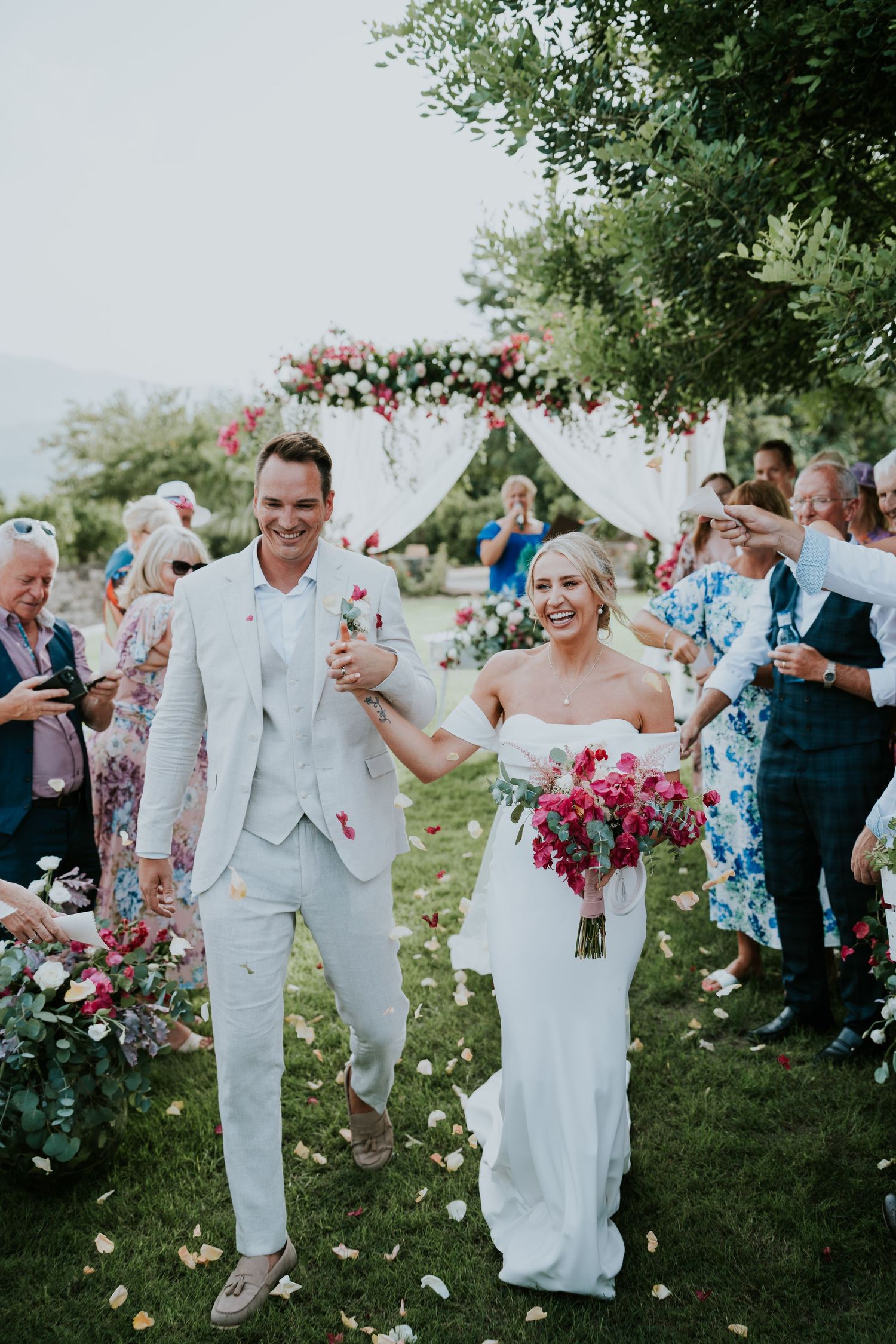 Newlyweds celebrate their ceremony exit while guests shower them with flower petals.