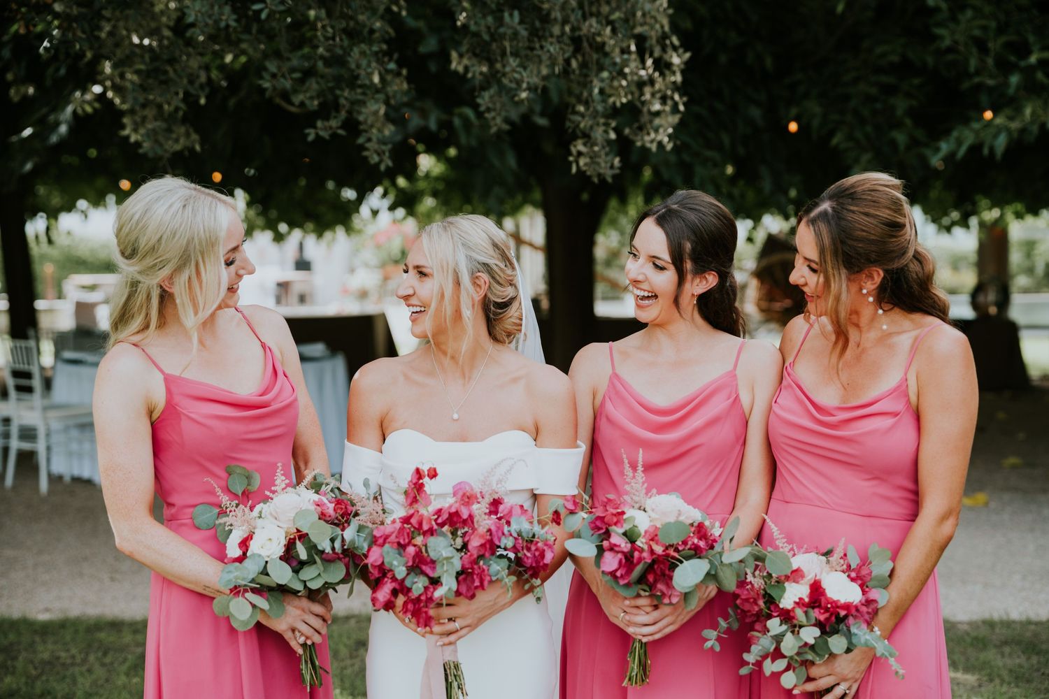 Wedding party poses with pink bouquets in matching pink dresses.