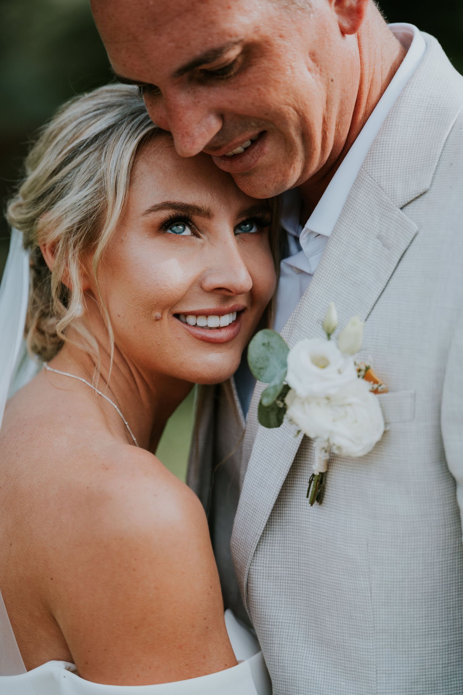 A close-up wedding portrait showing a couple in white attire with a delicate floral boutonniere.
