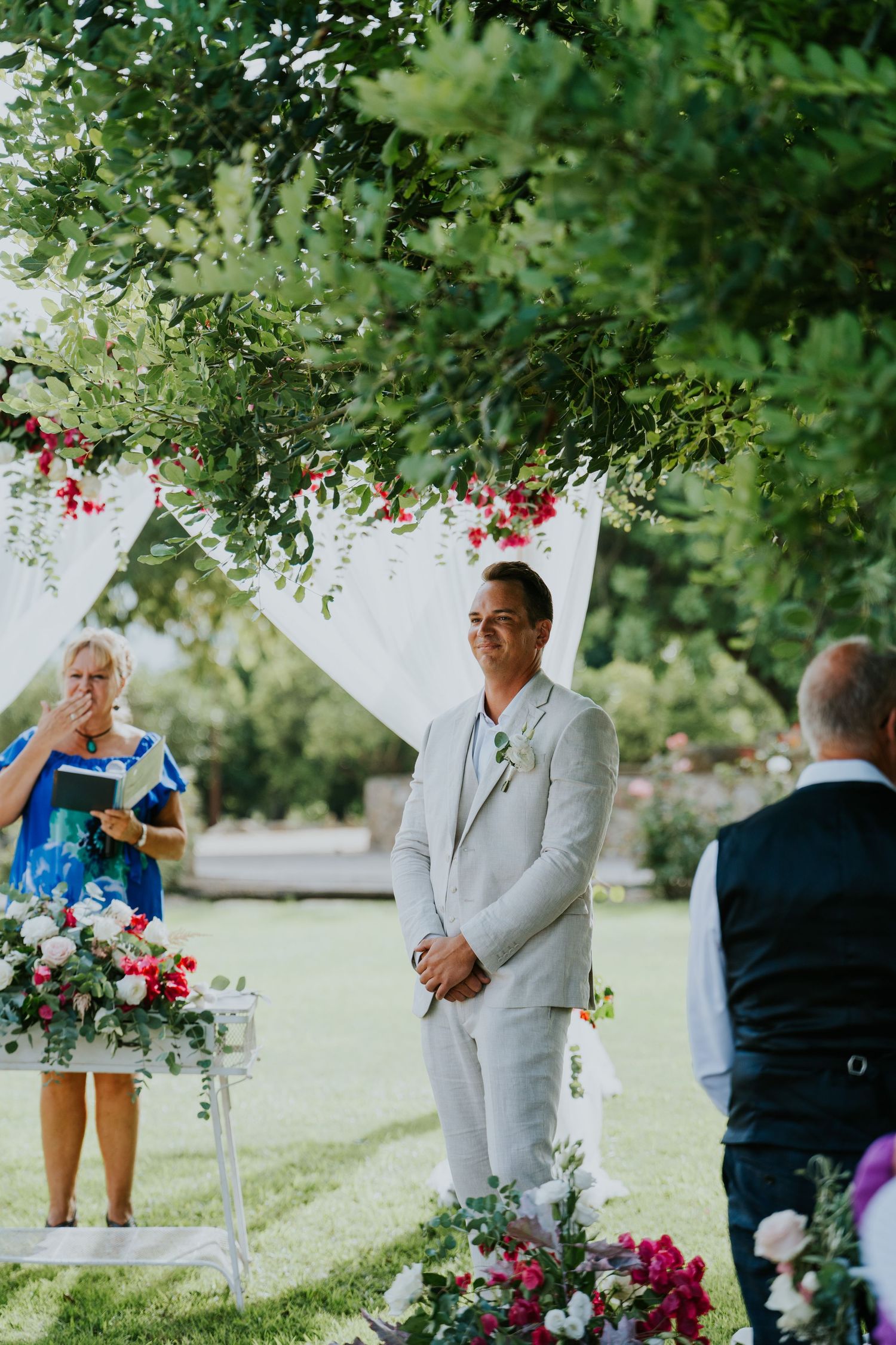 Wedding ceremony in progress under a decorated arch with florals and greenery.
