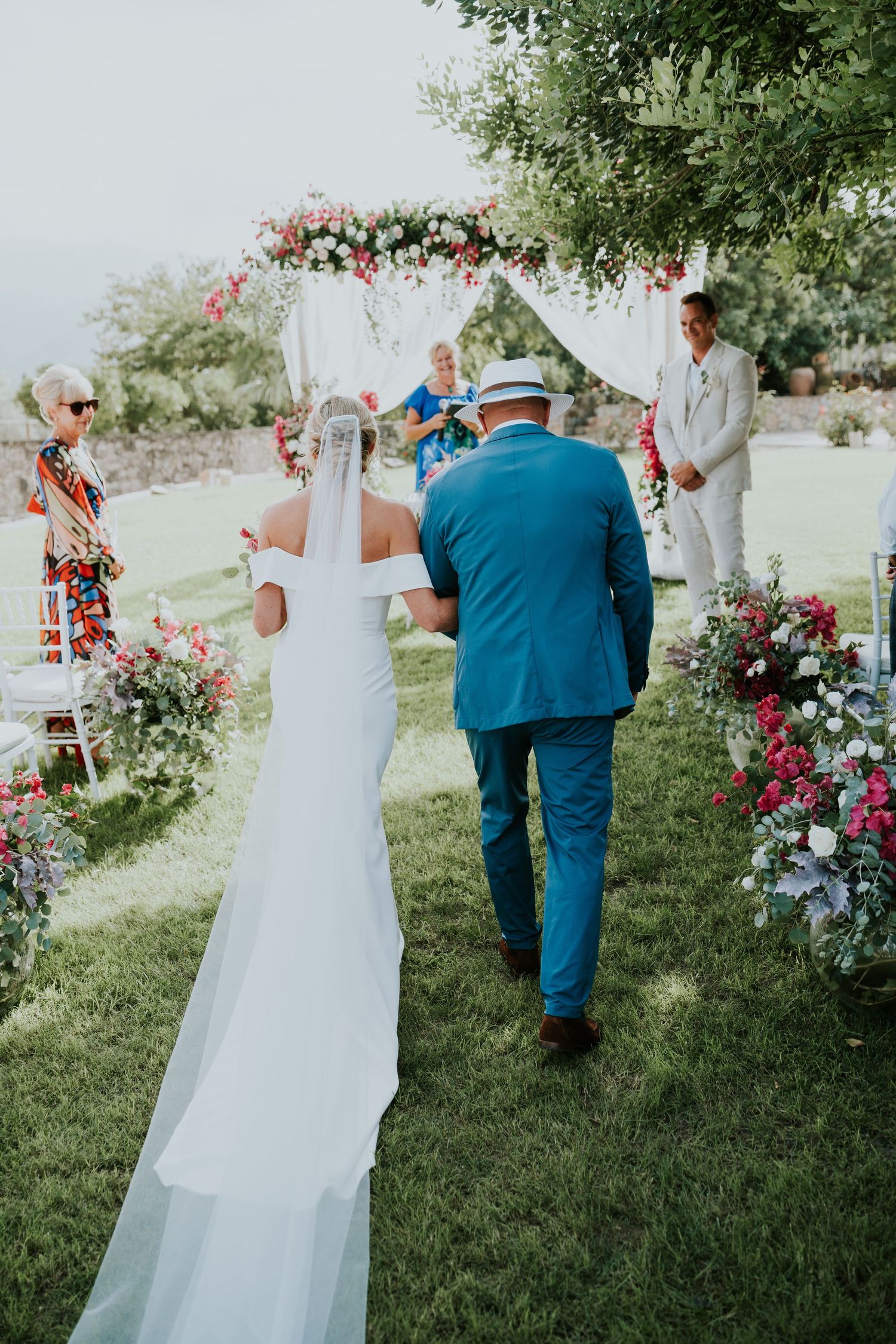Outdoor wedding ceremony under a floral arch with pink and white flowers.