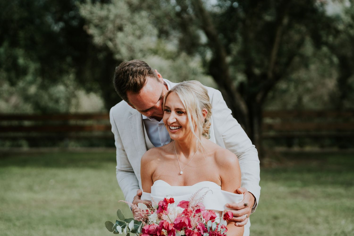 Romantic wedding portrait in a garden setting with bright red floral bouquet.