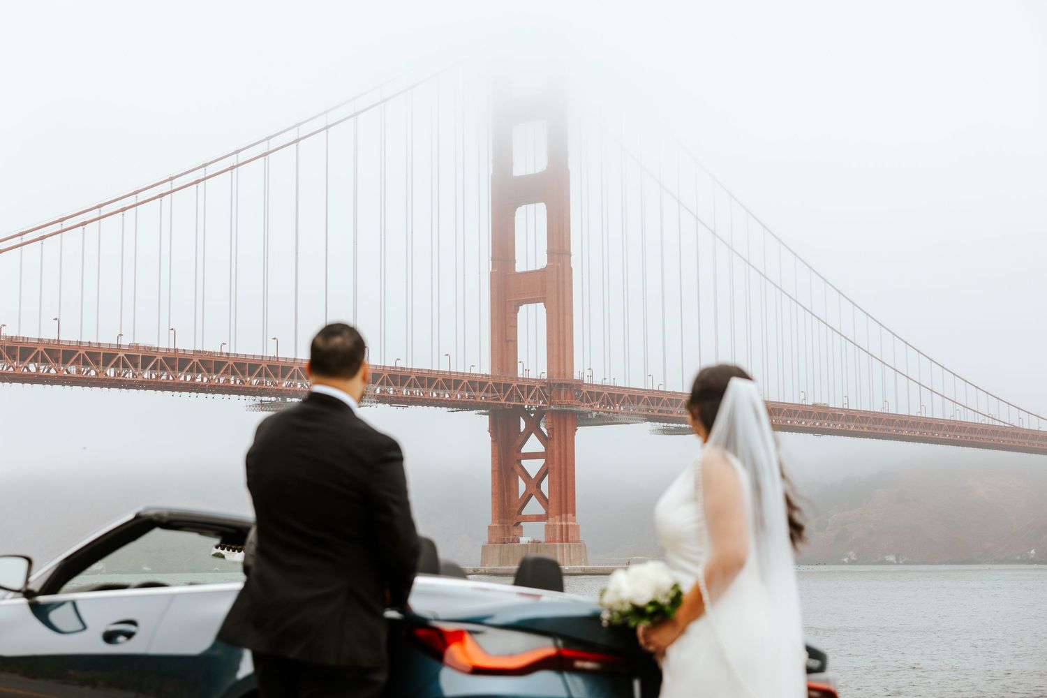 overcast foggy golden gate bridge with elopement couple standing in front of convertible car