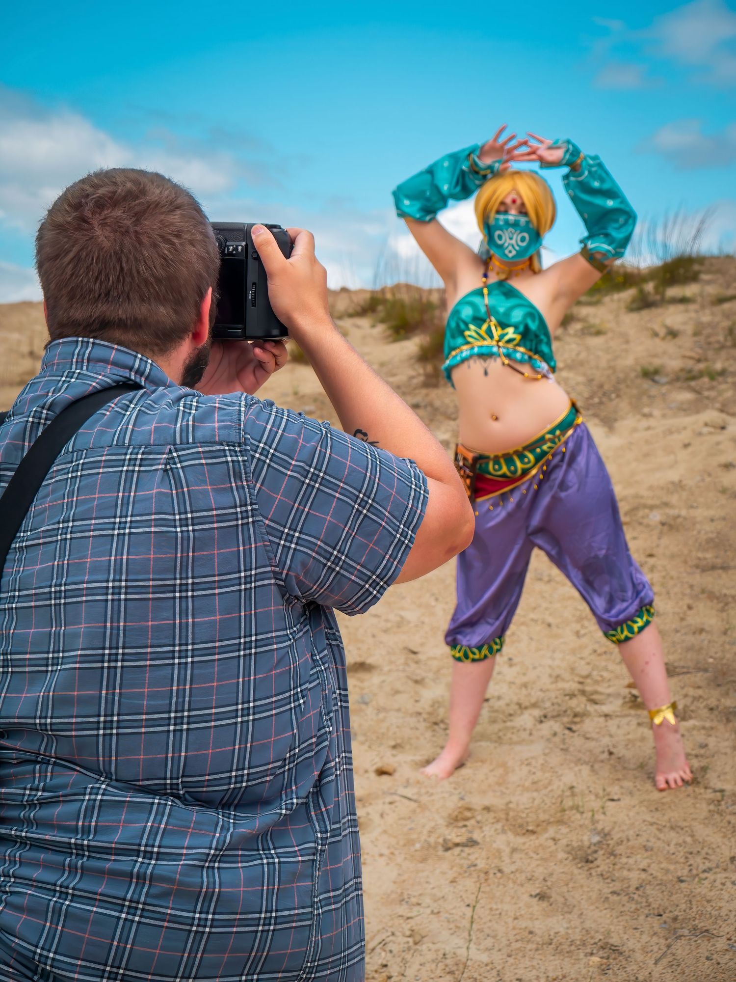 Photographer capturing dancer in colorful costume on sandy dunes.