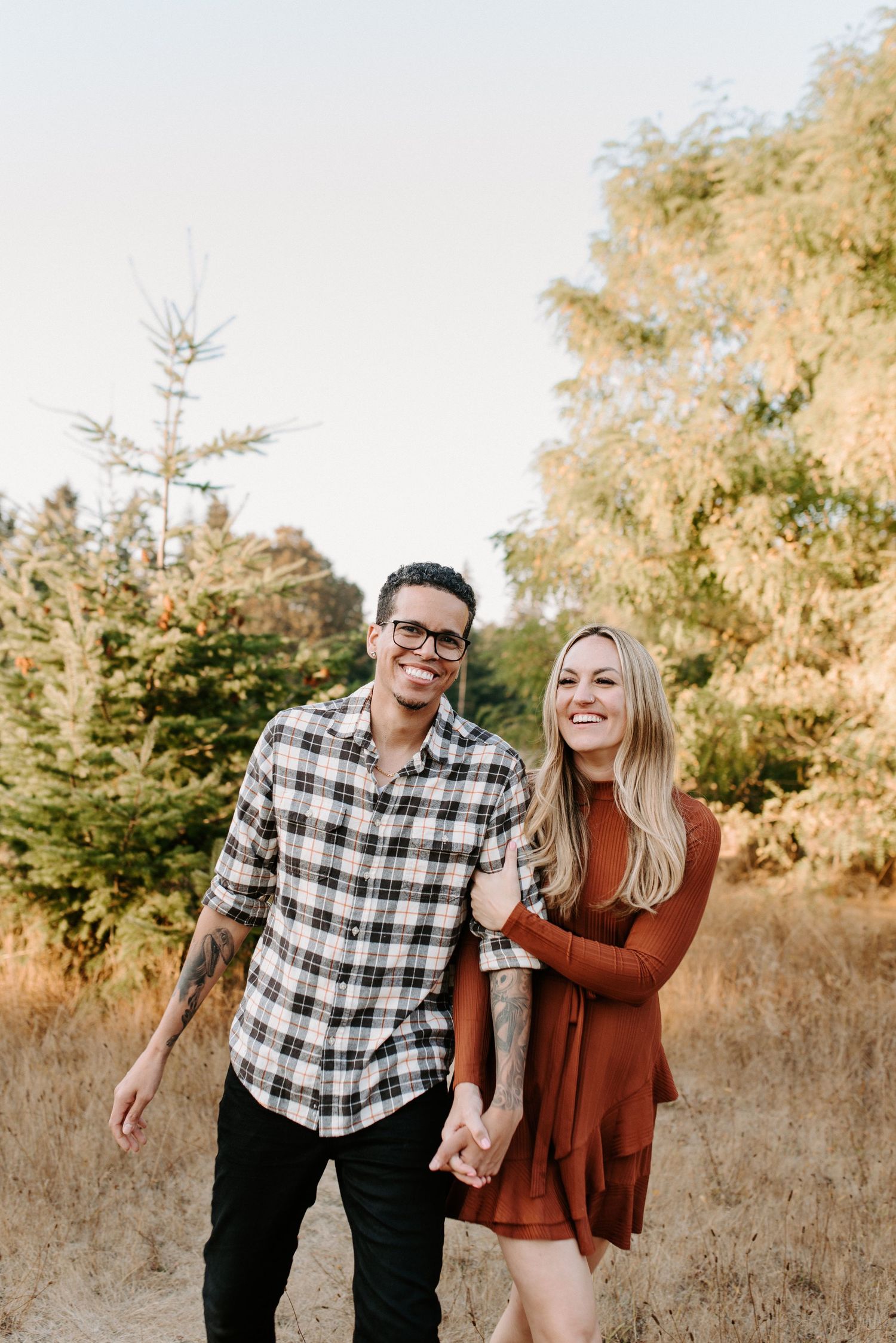 Playful couple laughing together in autumn field with evergreen trees.