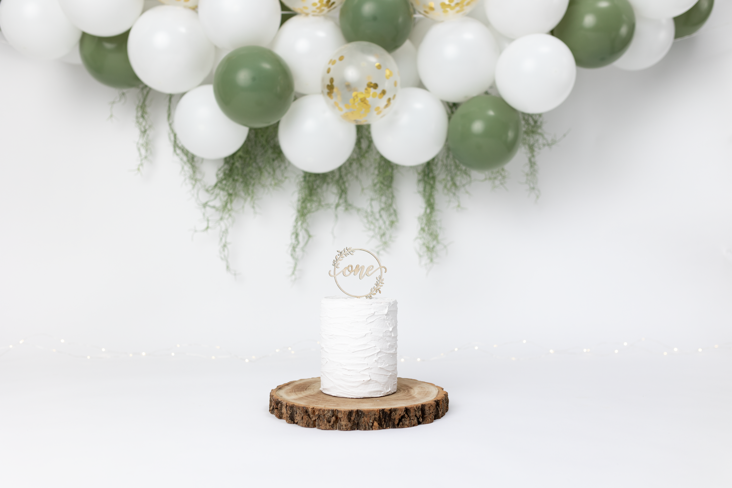 White and sage green balloon arch over wooden platform with decorative bottle.
