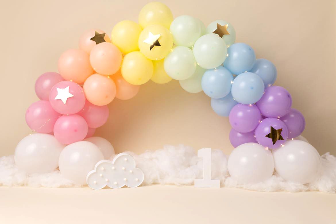 Pastel rainbow balloon arch with gold stars against neutral background for party decoration.