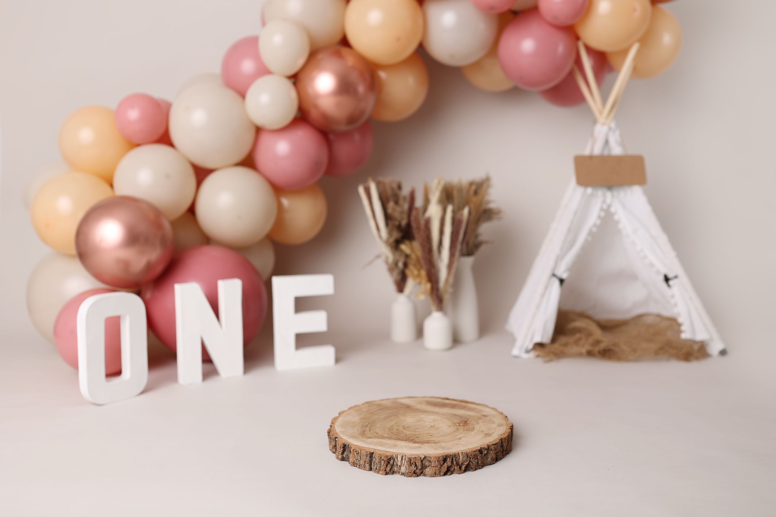 Boho themed first birthday decor with balloon arch, teepee and wooden accents.