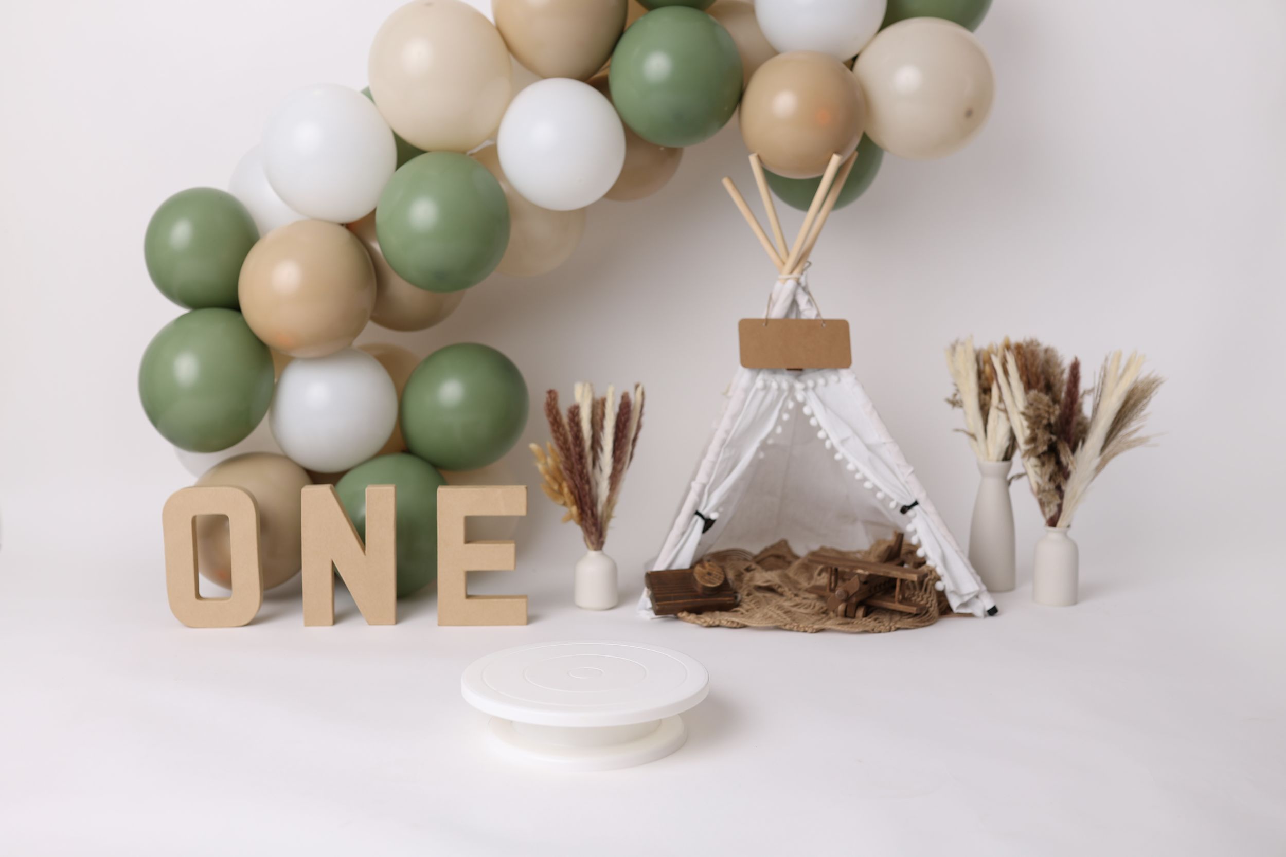 Minimalist first birthday setup with balloon garland, teepee and wooden 'ONE' letters.