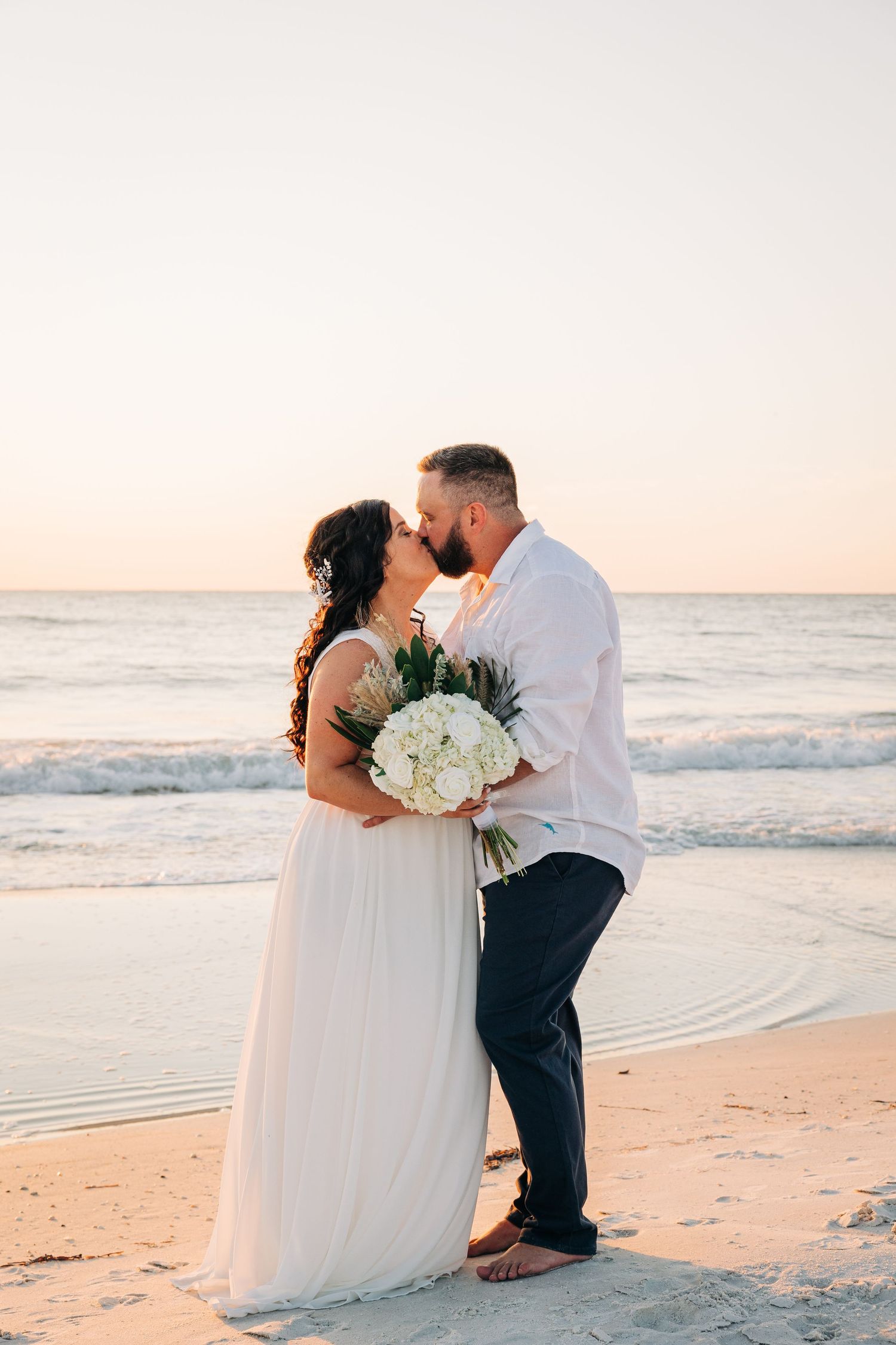 Bride and Groom kissing at sunset on Anna Maria Island Beach by Sarasota wedding photographer.