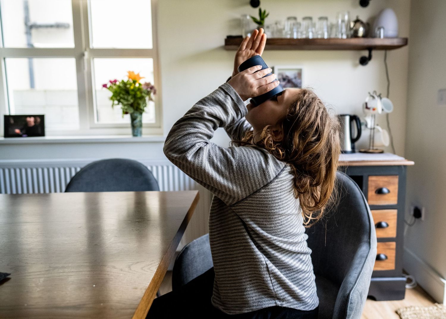 Person drinking directly from a bottle in a kitchen with natural light coming through the window.