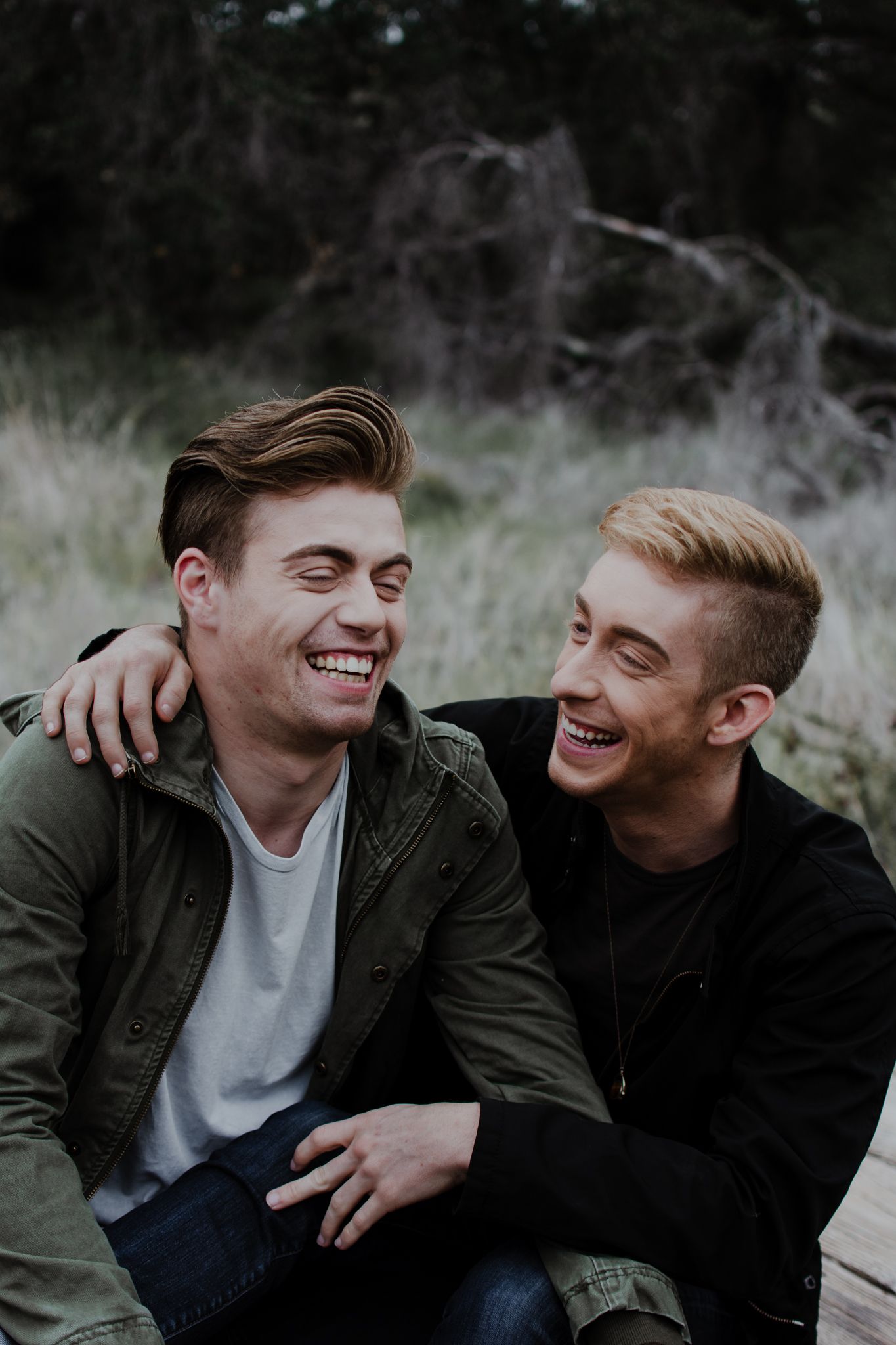 Close up of gay couple holding each other and laughing while seated on a wooden pathway in a field