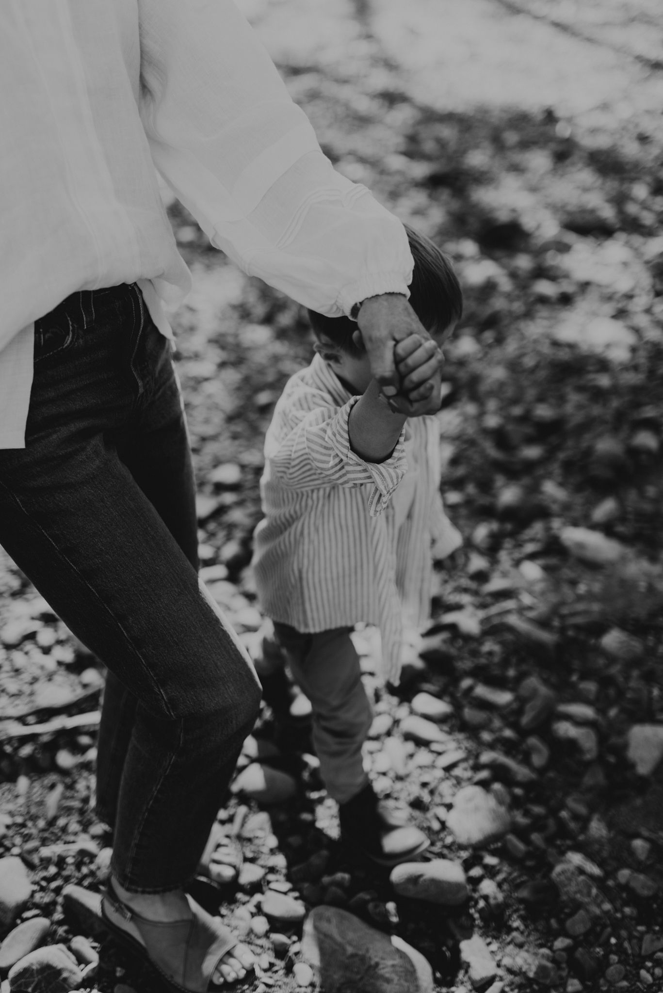 Black and white image of a parent helping a small child walk on rocky ground.
