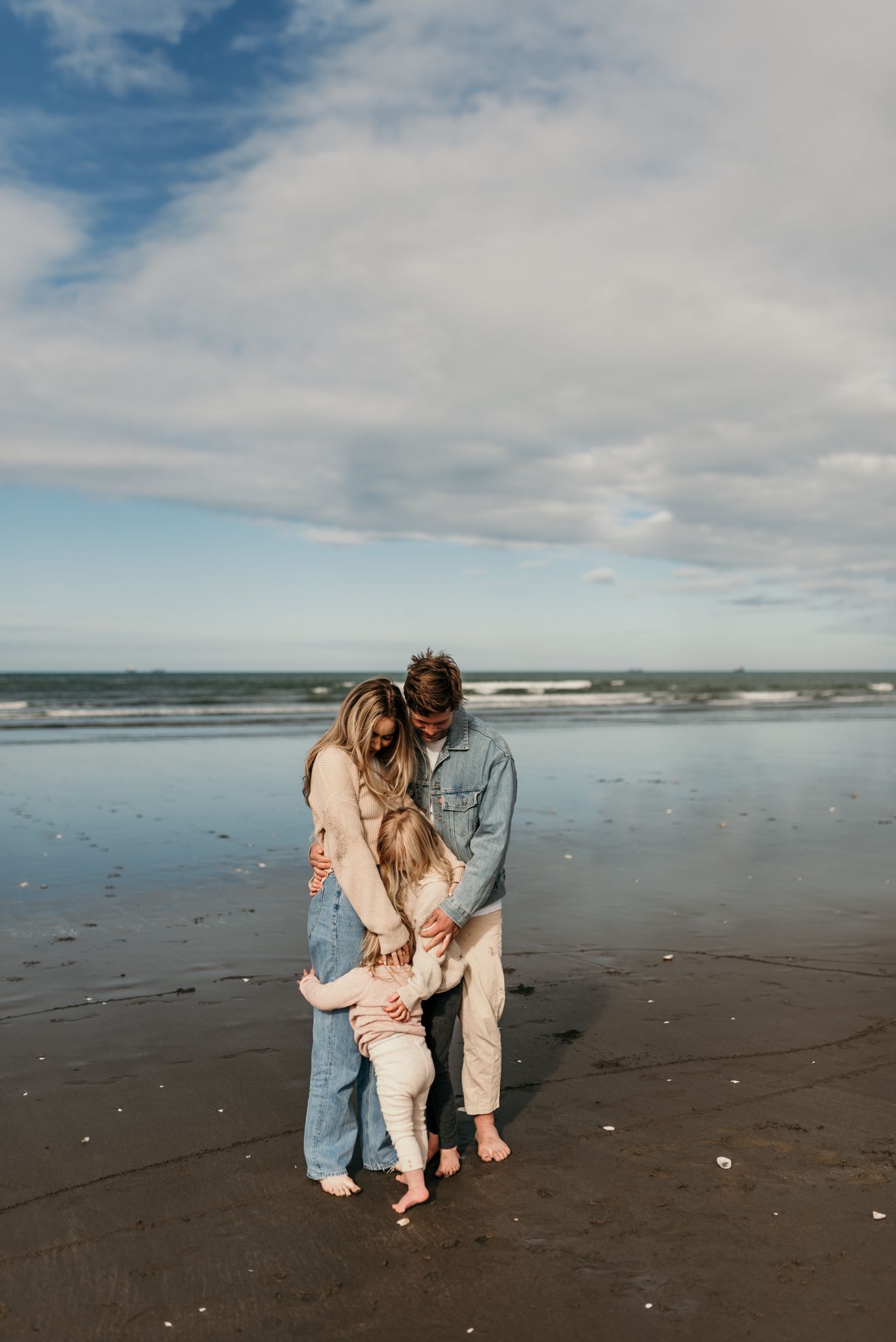 Family sharing an intimate moment together on a moody beach with waves in the background.