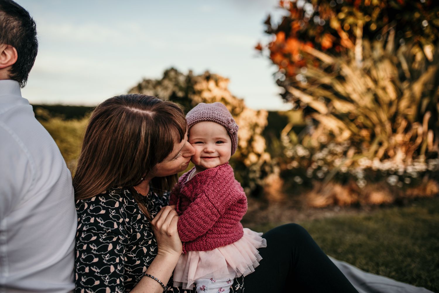 A joyful family moment captured outdoors with a small child in pink during golden hour.