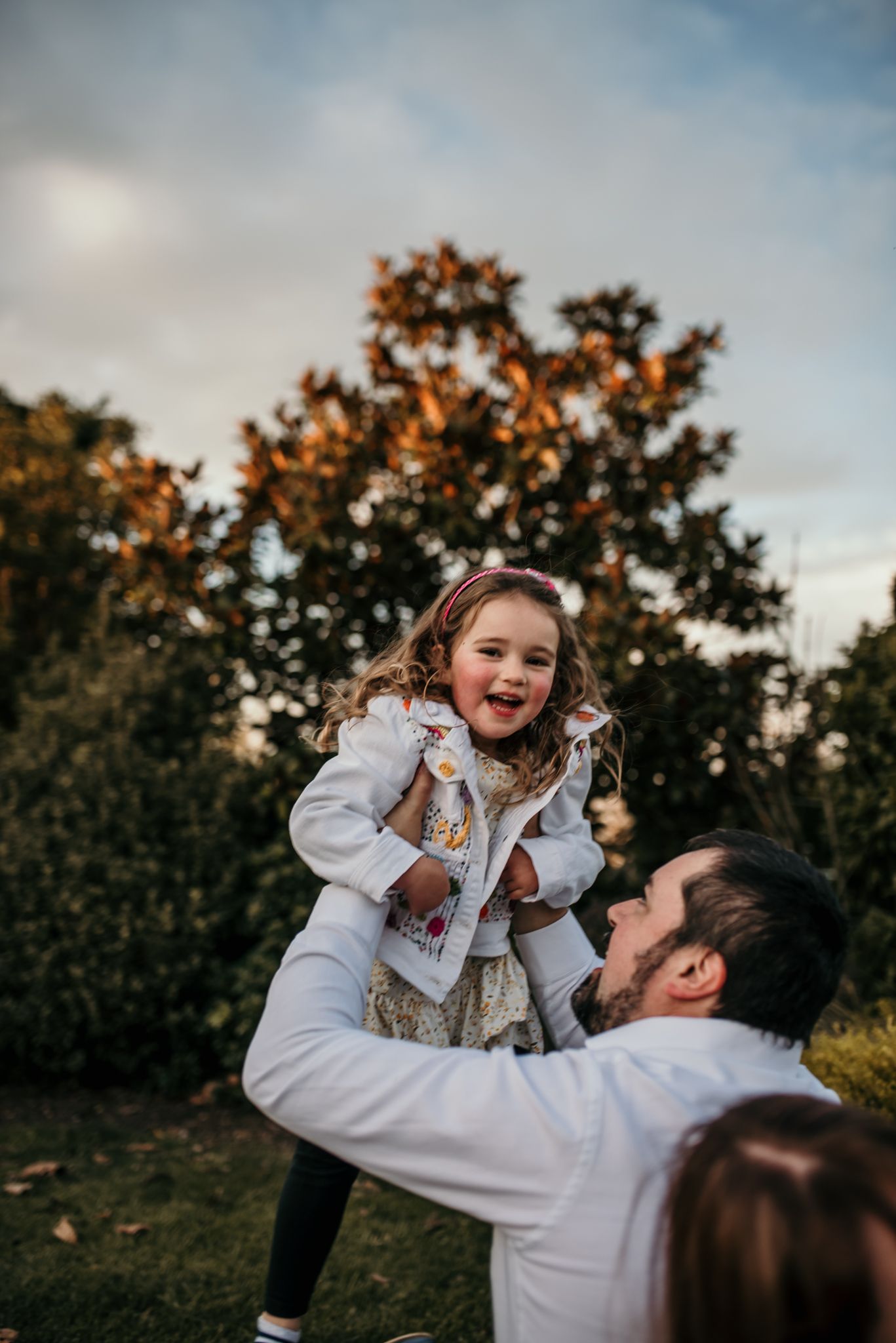 Playful family interaction in an autumn garden with a child being lifted high in the air.