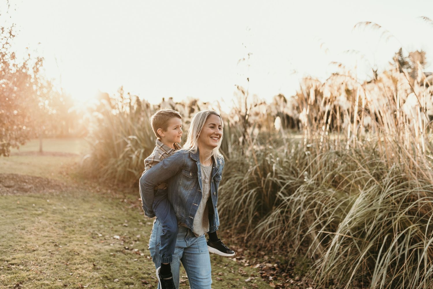 Parent carrying child piggyback style through a sunlit field at golden hour.