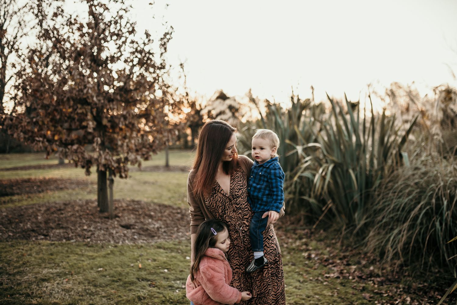 Family spending time together outdoors near tall ornamental grasses during sunset.