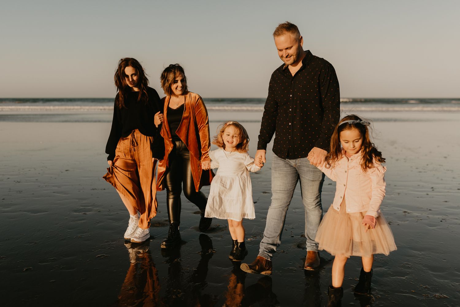 Group walking together on a moody beach at sunset wearing coordinated autumn outfits.
