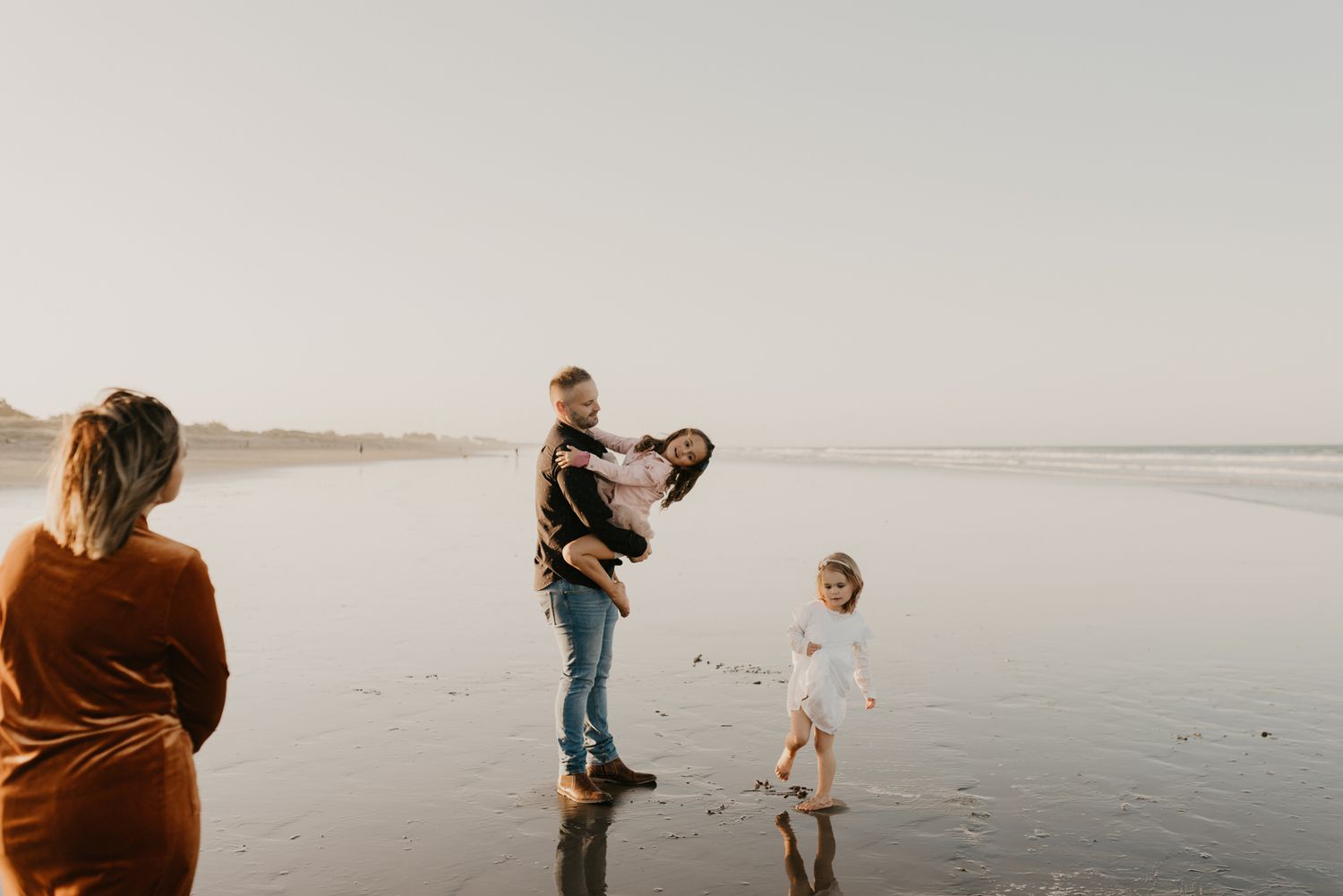 Family enjoying playful moments together on a misty beach at sunset.