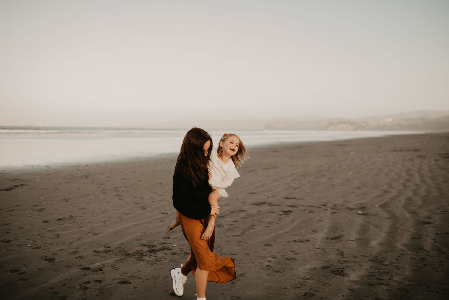 Joyful moment captured on a moody beach with dark sand and overcast skies.