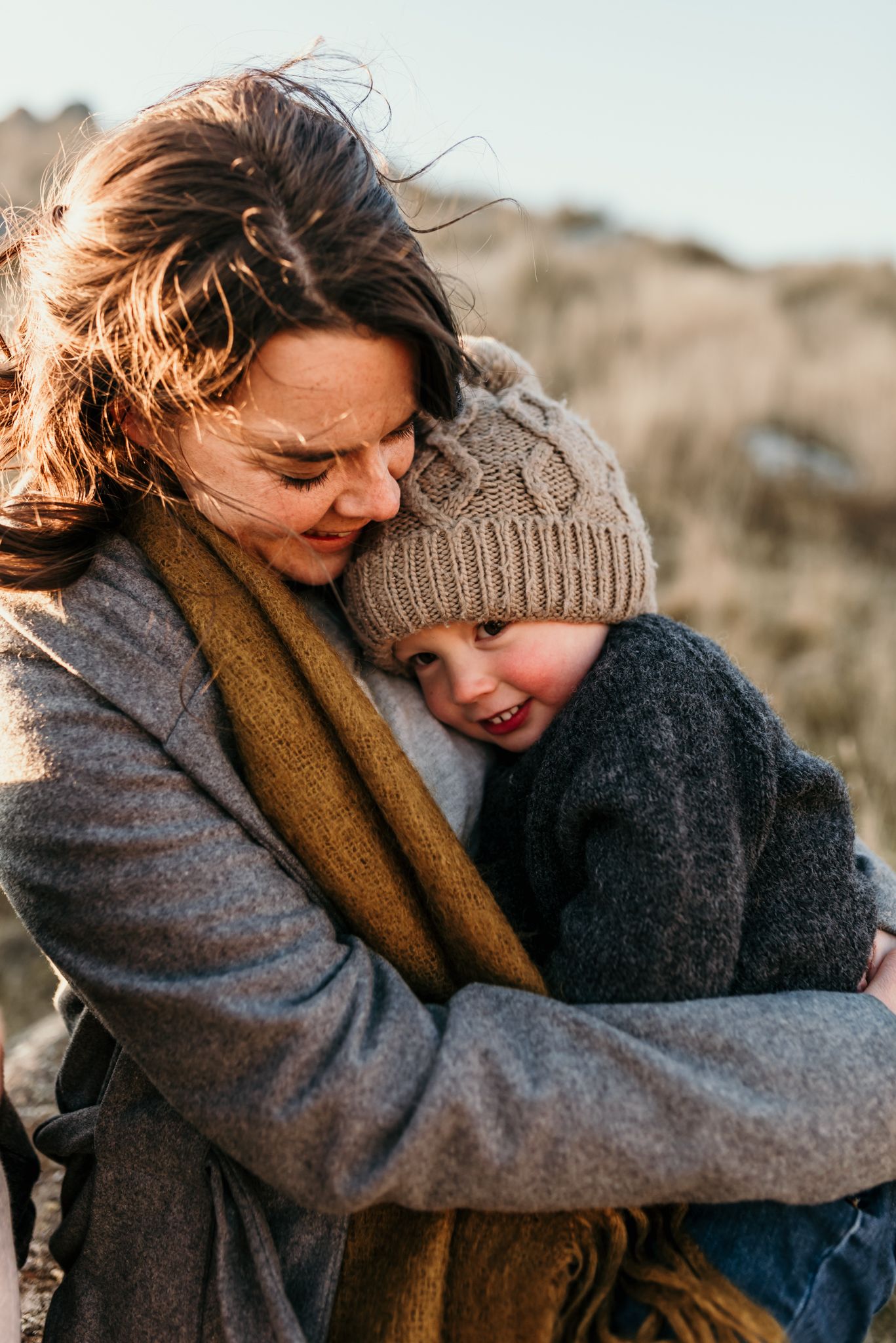 Tender embrace between parent and child wearing winter clothing outdoors in dramatic lighting.