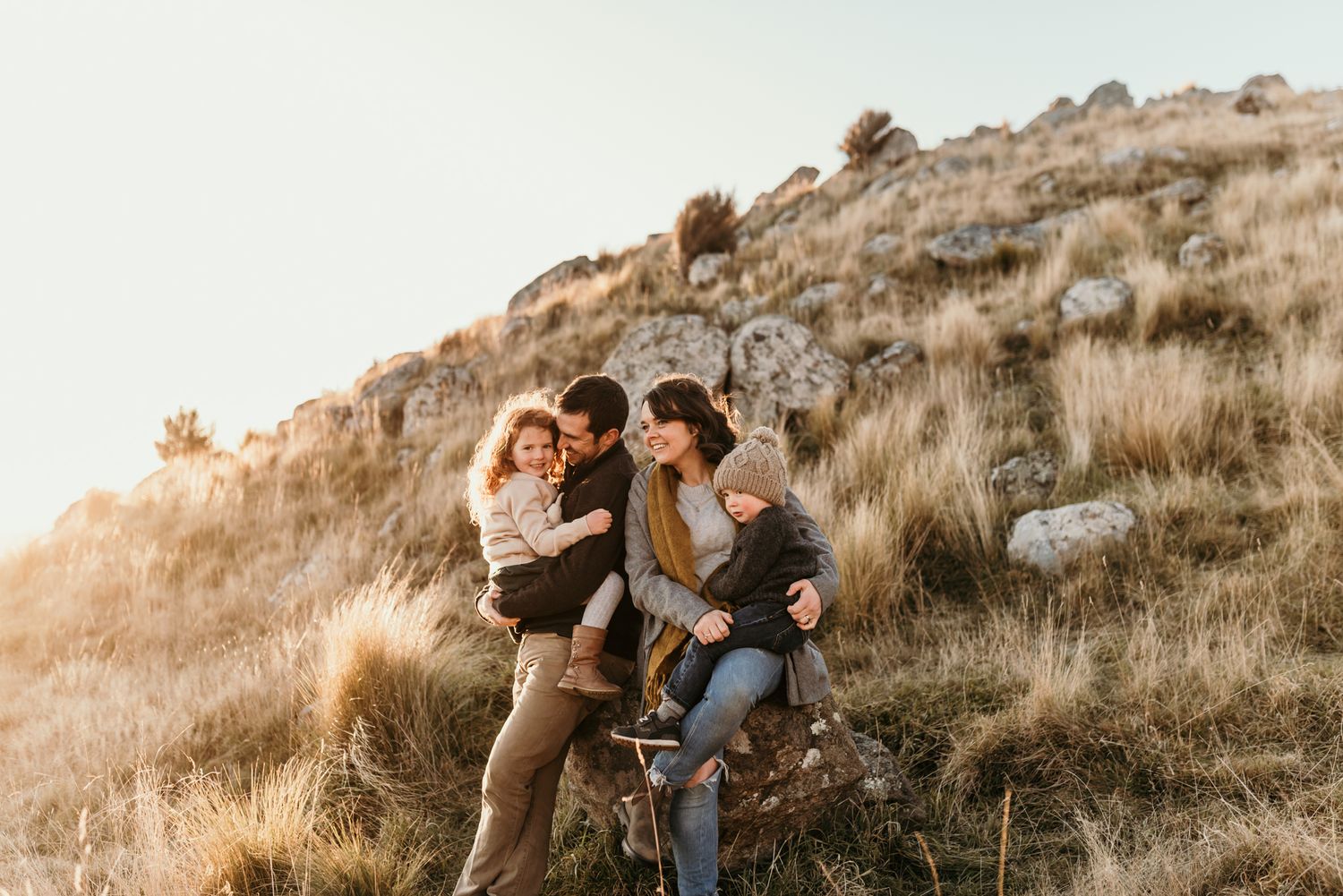 Family enjoying a playful moment together on a grassy hillside during golden hour.