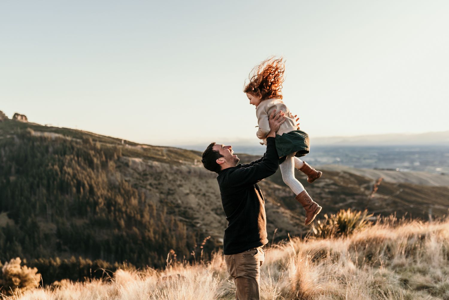 Joyful moment captured as figures play and spin on hilltop overlook at sunset.
