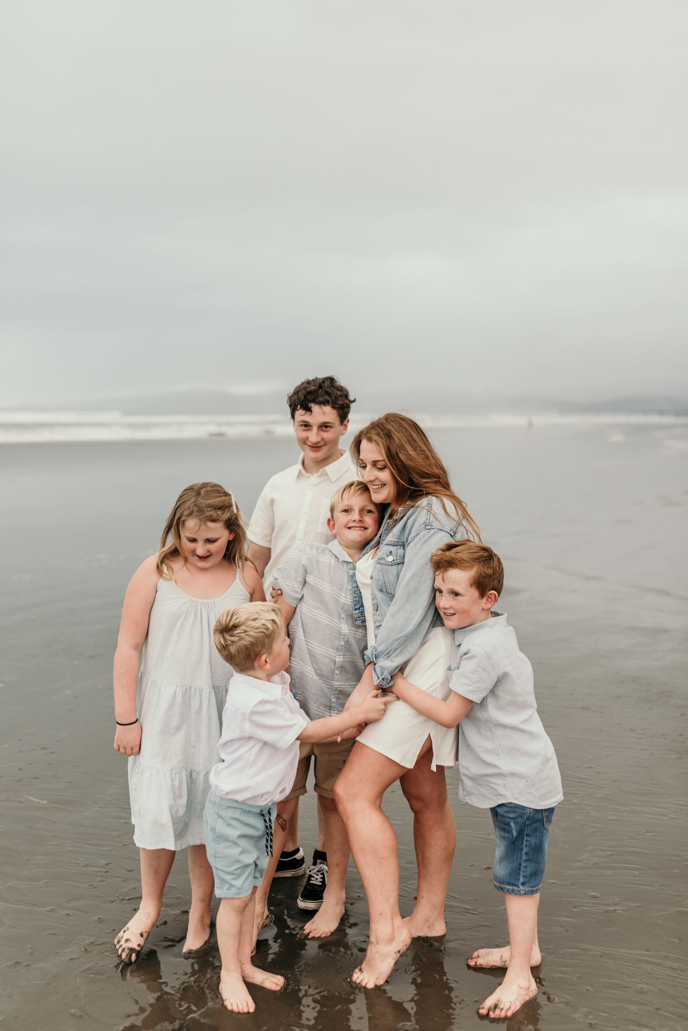 A warm family photo captured on a cloudy beach with everyone gathered close together.