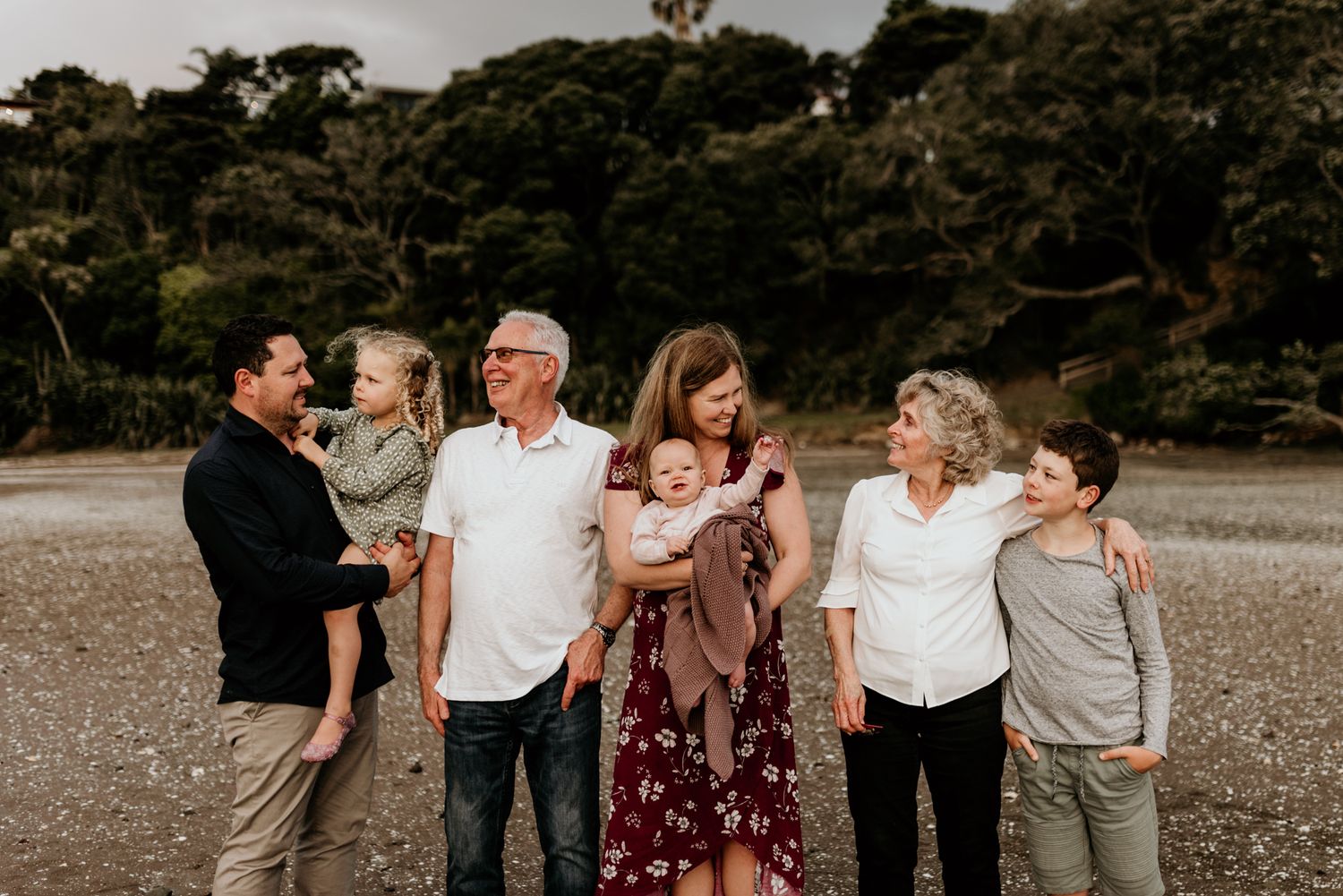 Extended family group portrait on beach with trees in background.