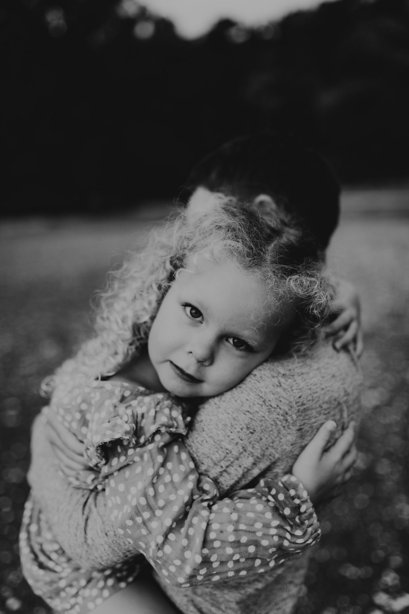 Black and white portrait of child hugging teddy bear outdoors.