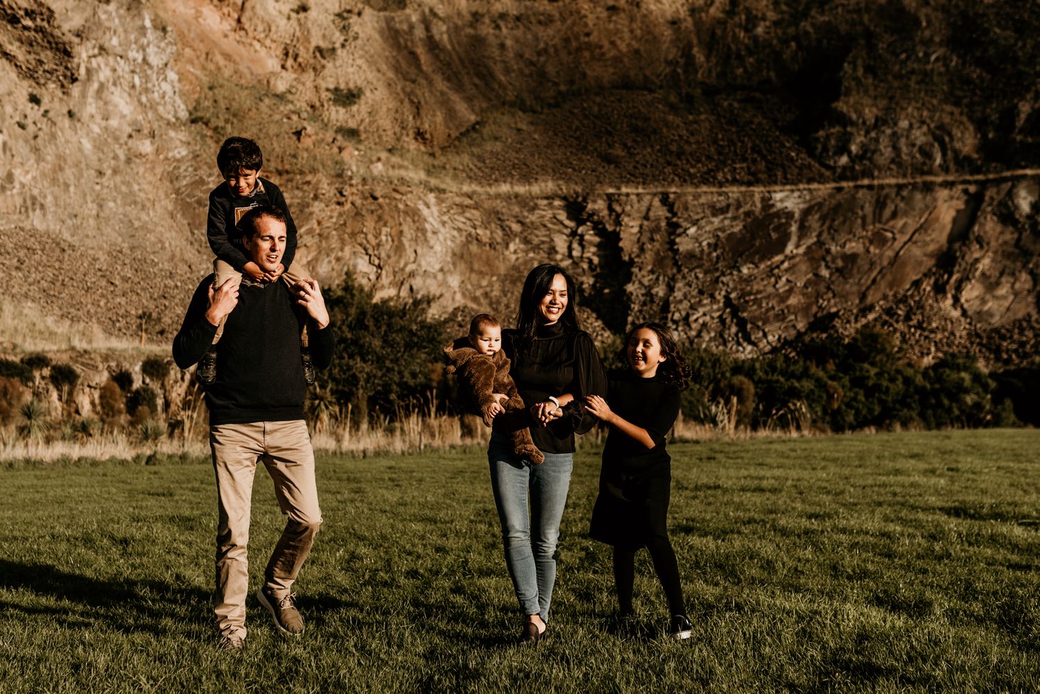 A joyful family group playing and walking together on grass with cliffs in the background.