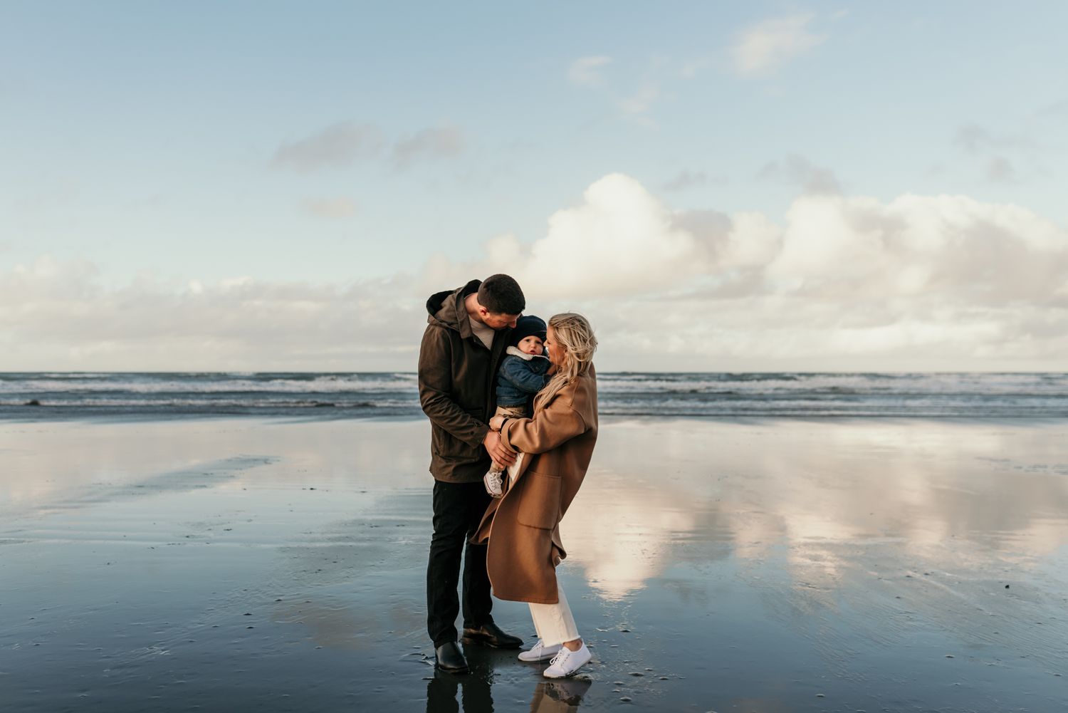 Romantic beach scene with couple embracing on wet sand as ocean waves roll in behind them.