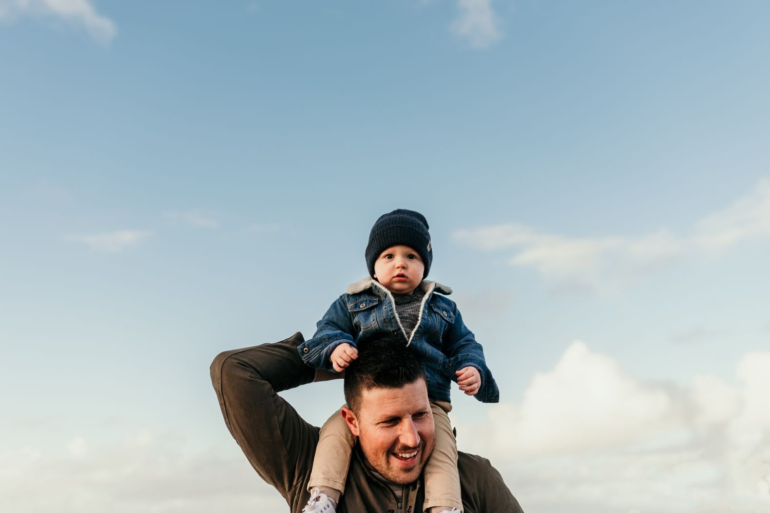 Playful shoulder ride moment captured against bright blue coastal sky.