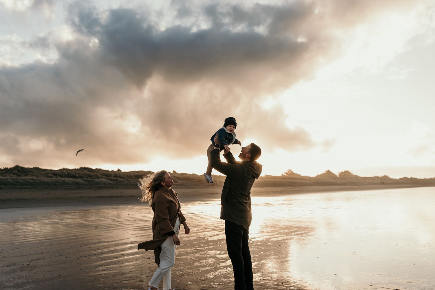 Family silhouetted against dramatic sunset sky on beach.
