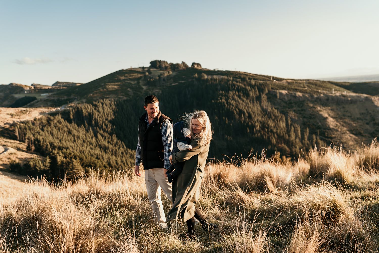 Family standing together on scenic hilltop with golden grass and mountain views.