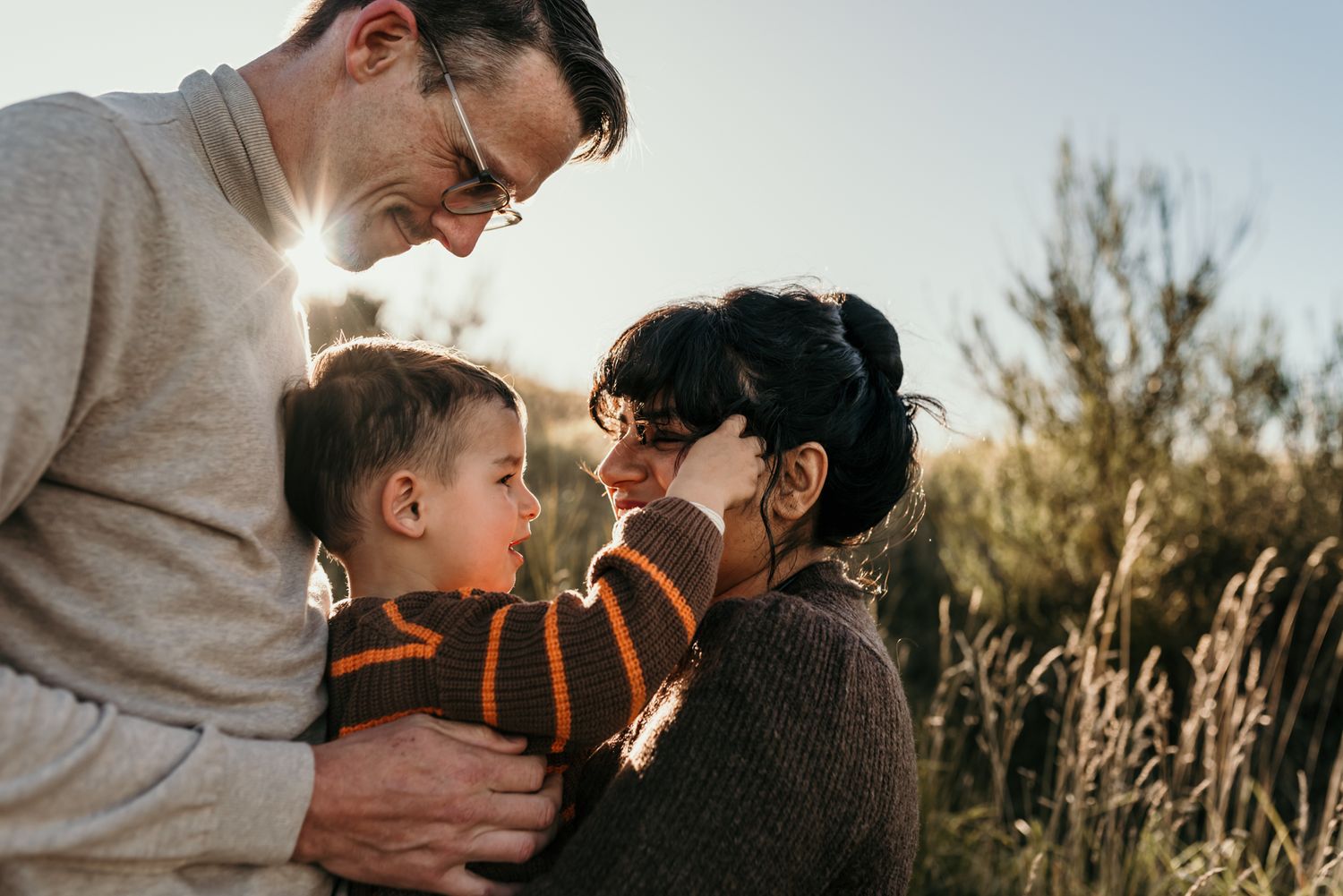 An intimate family moment captured in warm sunlight with natural scenery behind.