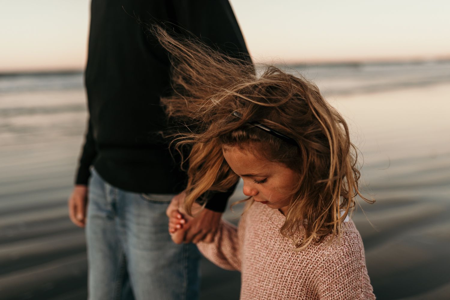 Wind-swept moment on beach with sunlit waves in background.