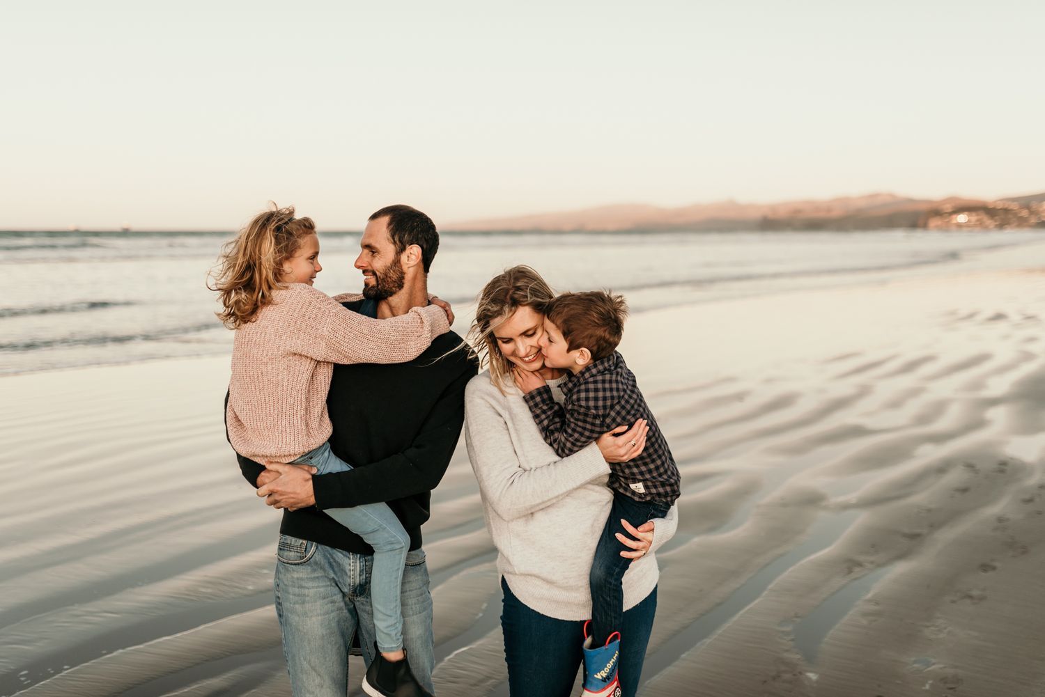 Family enjoying playful moment together on beach at sunset.