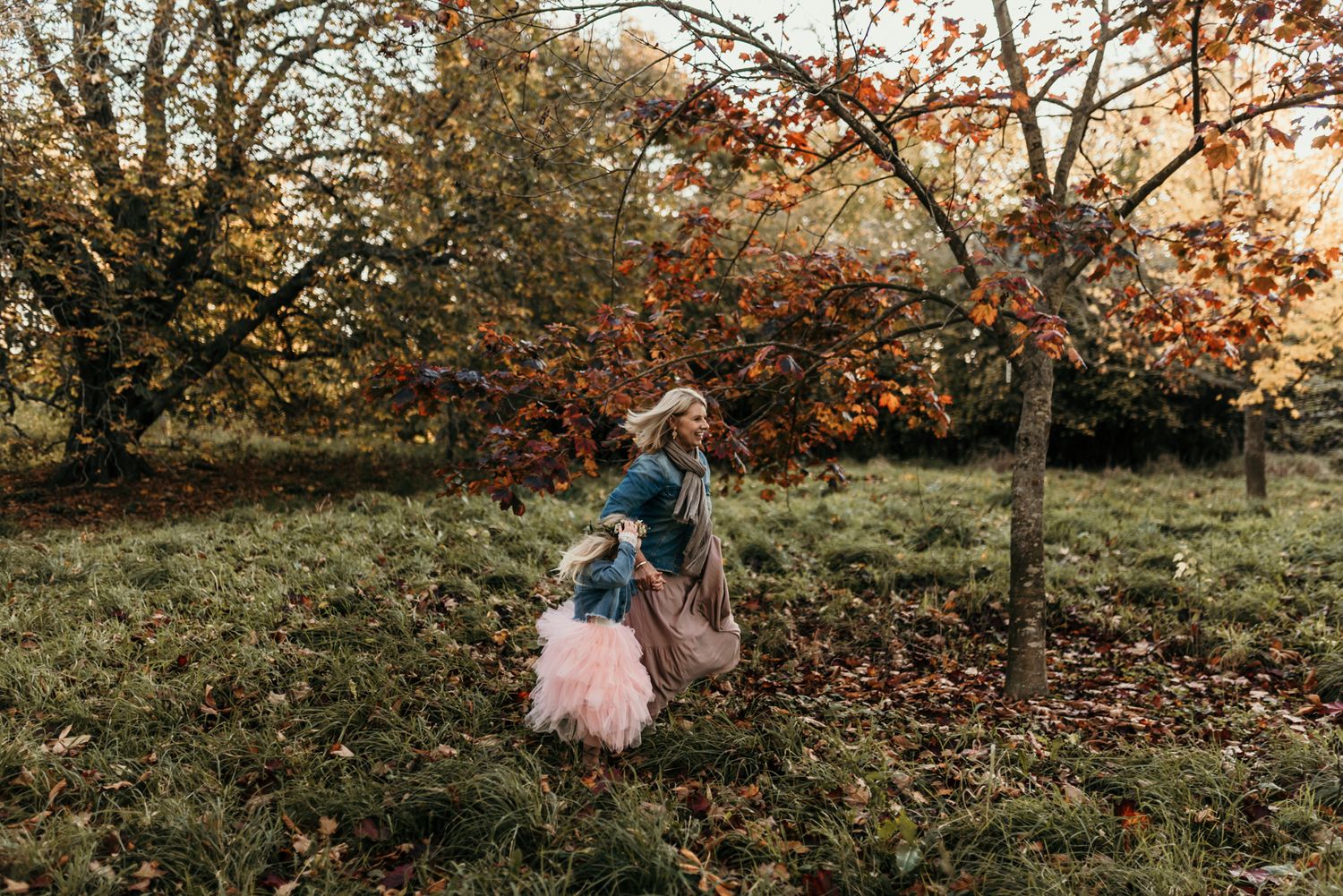 Child in a pink tutu being lifted high in the air during sunset in an autumn garden.