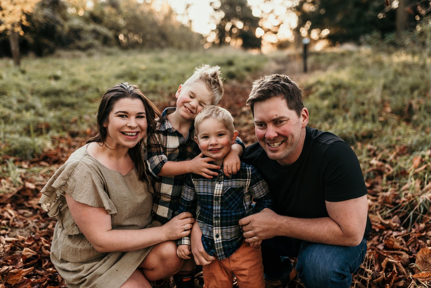 Family sitting together and smiling outdoors among fallen autumn leaves at sunset.