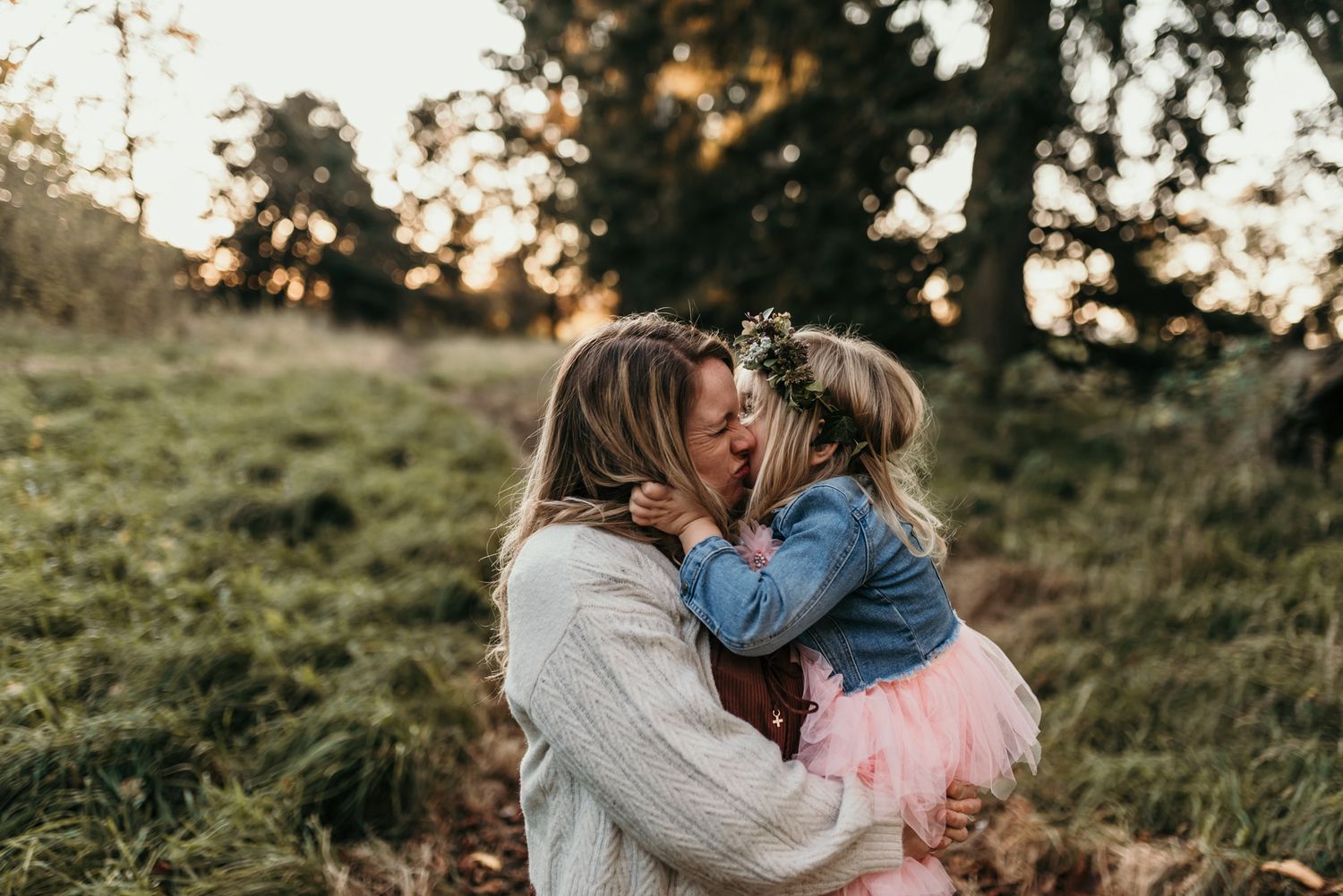 Mother and child sharing a tender moment together on a grassy hillside at sunset.