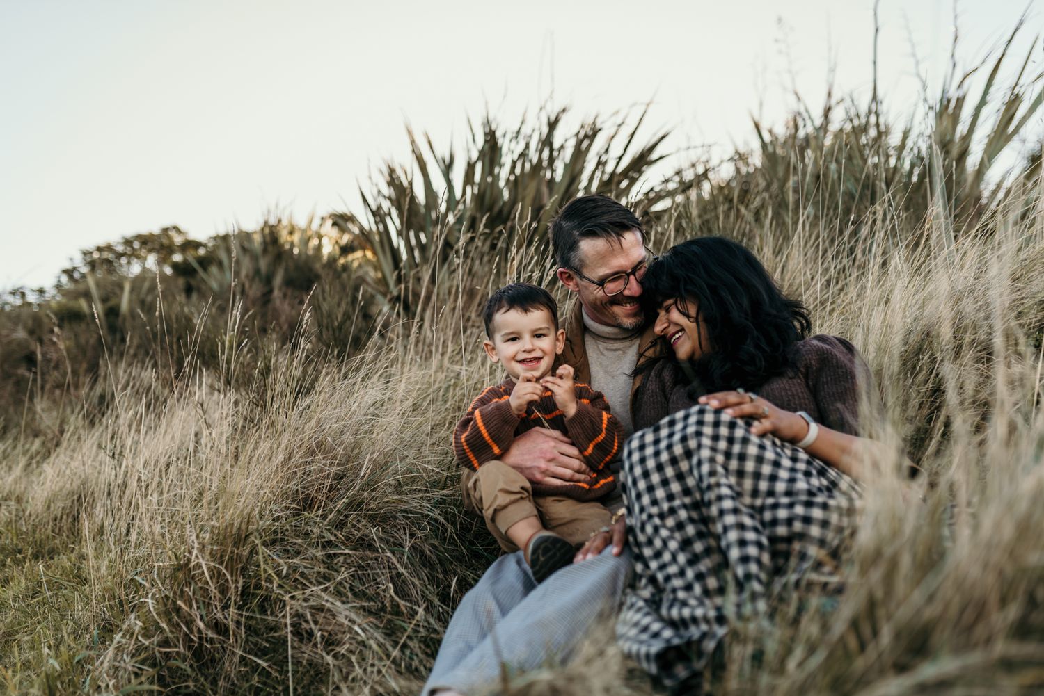 A tender family moment captured among tall grasses during sunset.