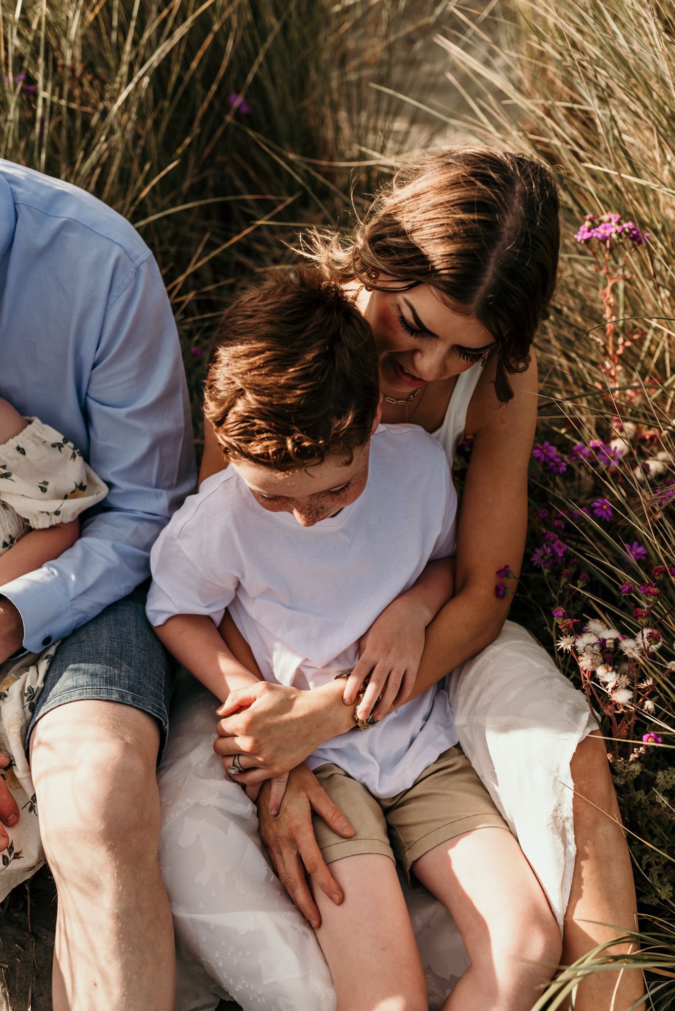 Tender family moment among tall grass and wildflowers on a sunny day.