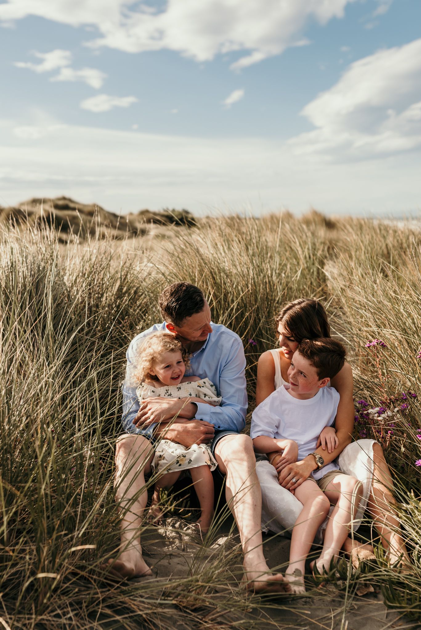 Family sitting together among beach grass on a sunny afternoon with blue skies overhead.