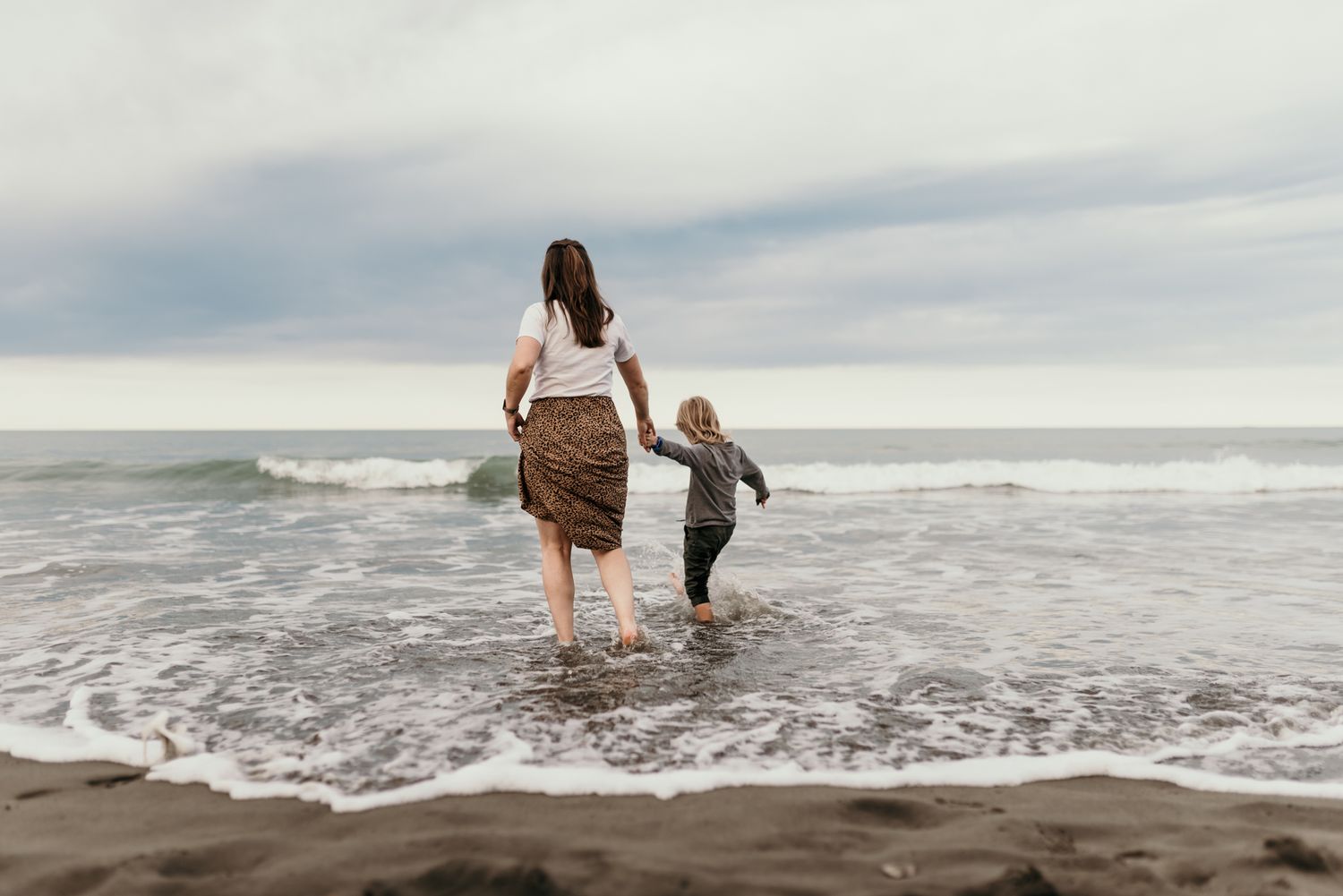 A tranquil scene of wading in shallow ocean waves on an overcast beach day.