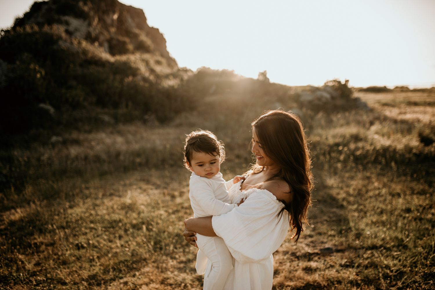 Silhouette of parent and child in white clothing against golden sunset light.