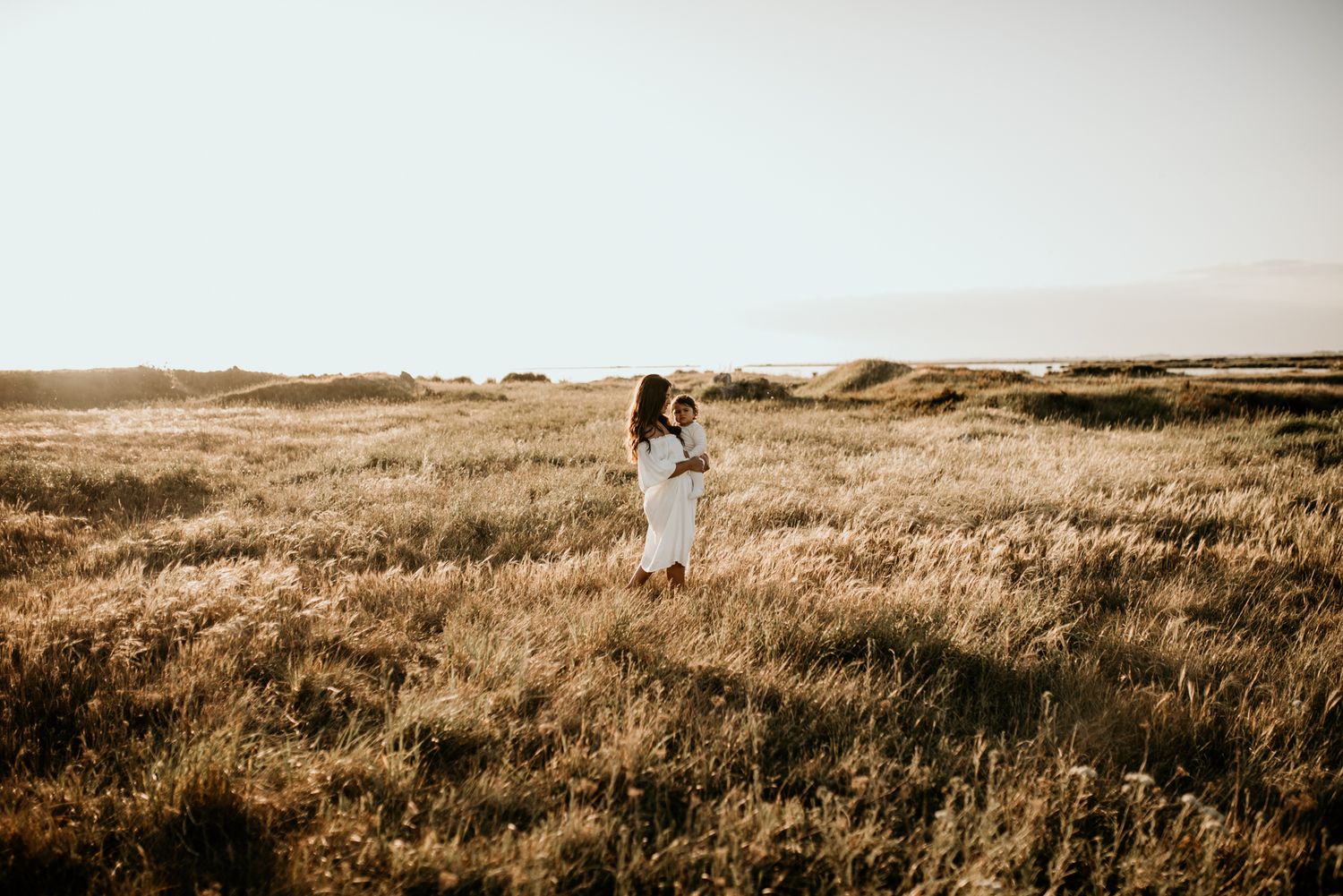 A figure in white dress stands alone in a vast golden prairie field.