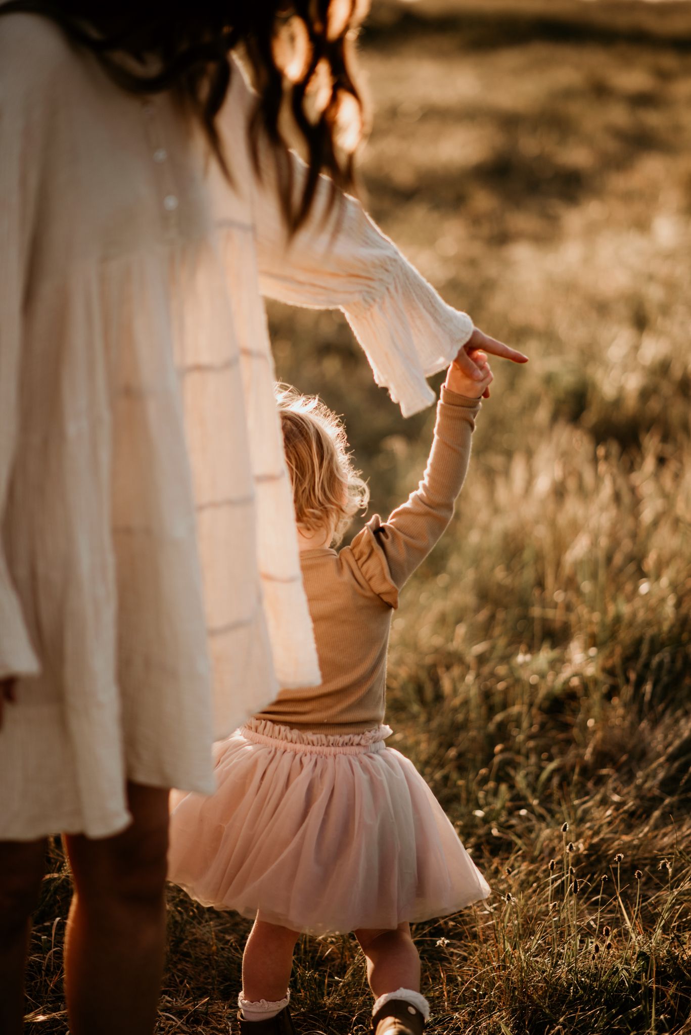 A child in tulle skirt holds onto flowing white fabric in golden sunlight.