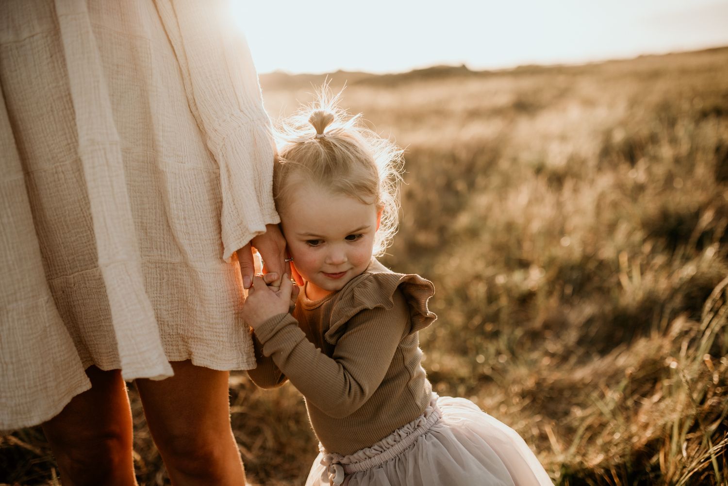 A small child in ruffled dress plays outdoors in warm evening light.